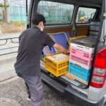 書籍が入ったピンク色の折りたたみコンテナを、ワゴン車の側面ドアから積み込もうとするスタッフ。