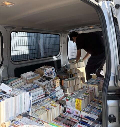 ハイエースの荷室いっぱいに積み込まれた大量の書籍をスタッフが整理している様子。