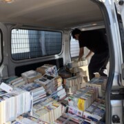 ハイエースの荷室いっぱいに積み込まれた大量の書籍をスタッフが整理している様子。