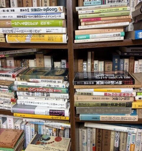 思想・哲学や専門書が並ぶ本棚と、棚の前に積み重ねられた書籍。